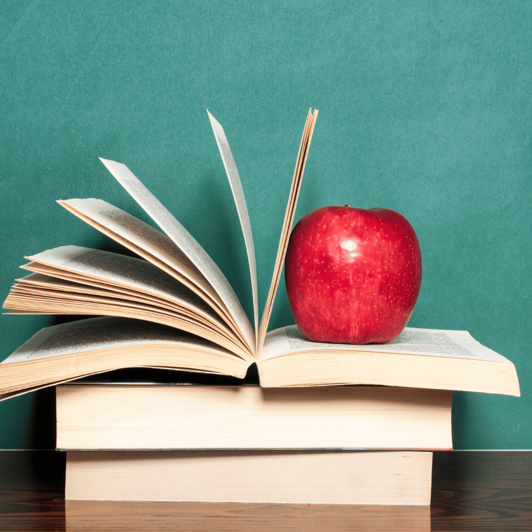 A stack of textbooks, one open with a red apple stacked on the open book. The image is used to describe cultural competency.